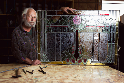 High quality stock photo of an active senior in his stained glass art studio.