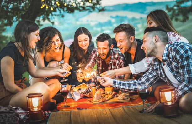 amici felici che si divertono con scintille di fuoco - giovani millennials accampati al picnic dopo il tramonto - giovani che si godono il vino alla festa barbecue estiva - concetto di amicizia giovanile sull'umore notturno - friendship camping night campfire foto e immagini stock