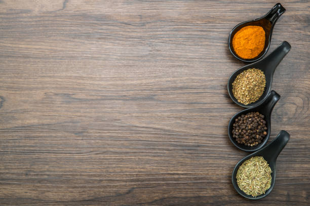 different spices and herbs in spoons or bowls on a brown wooden background . food and cuisine ingredients with copy space .dried rosemary,black pepper,red paprika powder or cayenne pepper ,oregano - oregano freshness herb brown imagens e fotografias de stock