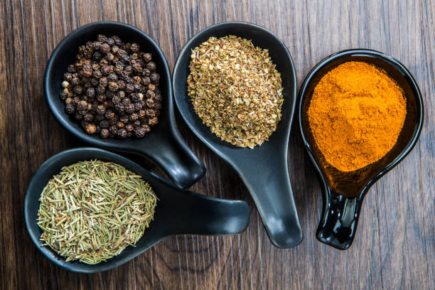 different spices and herbs in spoons or bowls on a brown wooden background . food and cuisine ingredients  .dried rosemary,black pepper,red paprika powder or cayenne pepper ,oregano - oregano freshness herb brown imagens e fotografias de stock