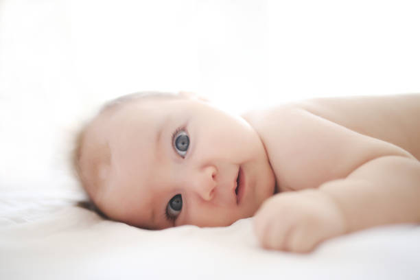 A three month old baby boy with blue eyes looks intently on an orange mat