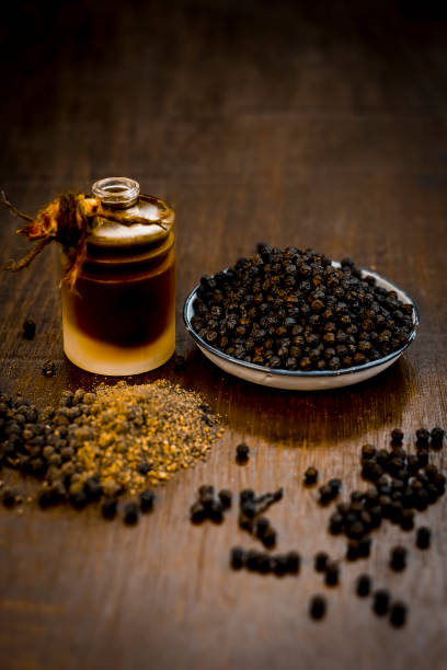 Close up of black peppercorns or kali mari on wooden surface with its extracted herbal beneficial oil. Close up of black peppercorns or kali mari on wooden surface with its extracted herbal beneficial oil. traditional musician stock pictures, royalty-free photos & images