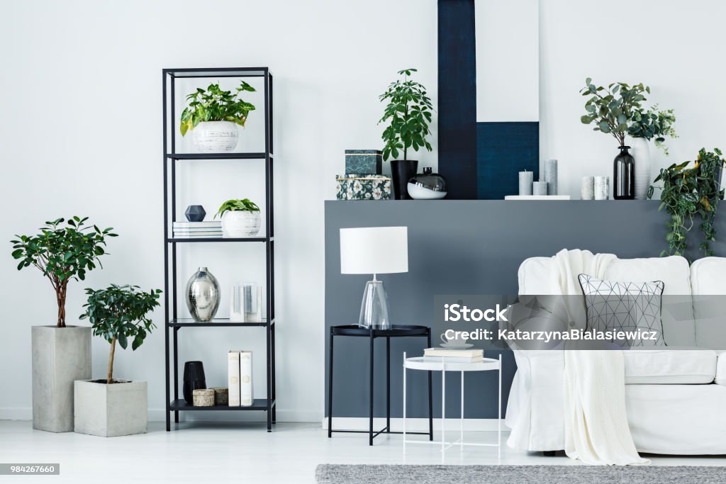 Two metal end tables Two black and white metal end tables with lamp, books and tea cup standing in bright living room interior with fresh plants, couch and decor Living Room Stock Photo