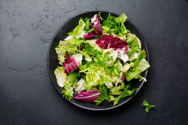 istock Fresh leaves of different salads in ceramic plate on black stone background. Selective focus. Top view. Copy space. 984289300
