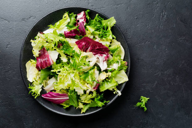 istock Fresh leaves of different salads in ceramic plate on black stone background. Selective focus. Top view. Copy space. 984289378