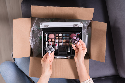 High Angle View Of A Woman's Hand Holding Cosmetics From Cardboard Box