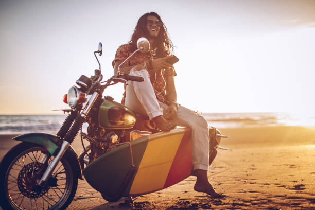Man sitting on a motorcycle at the beach while using phone