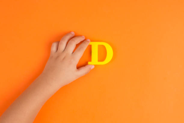 Little baby boy hand showing the letter D Little baby boy hand showing the letter D on orange paper background. magnetic letter stock pictures, royalty-free photos & images