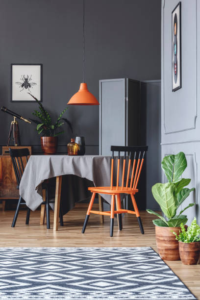 istock Dining room interior with a table, black and orange chairs, plants and patterned carpet 984519932