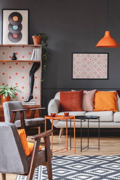 istock Retro living room interior with armchairs, sofa decorated with orange pillows, coffee table, poster, cupboard and patterned carpet 984519962