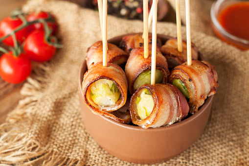 Bacon wrapped brussels sprouts served with cherry tomatoes in ceramic bowl. Appetizer rolls