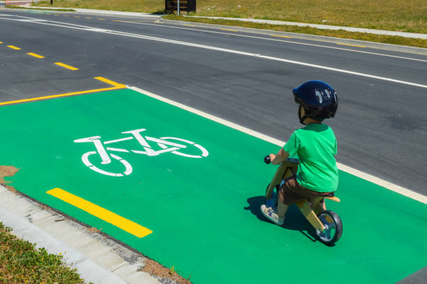 A photograph of a 2-year old riding a balance bike along a bike lane.