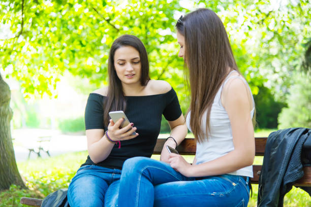 istock Two beautiful girls in the park surf the web. 984629482