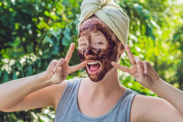 Photo of Face Skin Scrub. Portrait Of Sexy Smiling Female Model Applying Natural Coffee Mask, Face Scrub On Facial Skin. Closeup Of Beautiful Happy Woman With Face Covered With Beauty Product. High Resolution