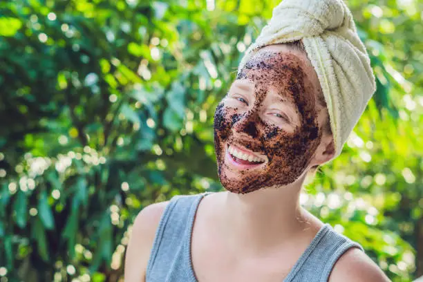Face Skin Scrub. Portrait Of Sexy Smiling Female Model Applying Natural Coffee Mask, Face Scrub On Facial Skin. Closeup Of Beautiful Happy Woman With Face Covered With Beauty Product. High Resolution.