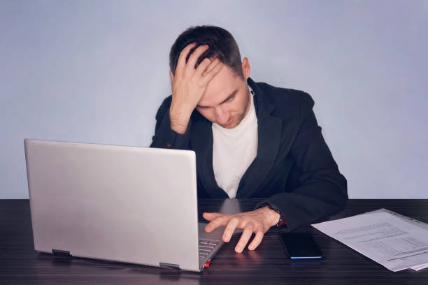 istock Serious frustrated businessman suffering from headache migraine at workplace. Feeling tired exhausted. Chronic work stress. Not a determined man holding his head and wants to press a button on laptop 984637494