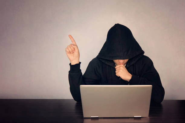 istock Hacker hooded in front of his computer show finger. Dark face. hooded .technology concept, hacker points finger at empty space for text. 984637790