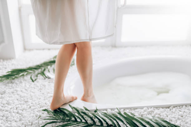 istock Woman in white bathrobe dips legs into the bath 984670982