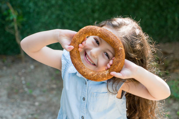 Adorable little girl holding Turkish Bagel (simit) Adorable little girl holding Turkish Bagel (simit) eating child cracker asia stock pictures, royalty-free photos & images