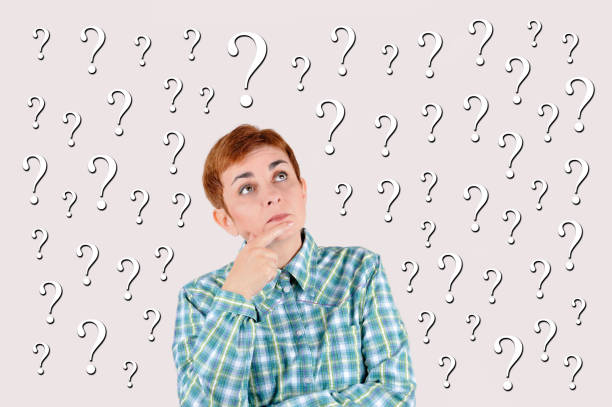 Young woman in pajamas sitting on floor and leaning on a question mark isolated on white background