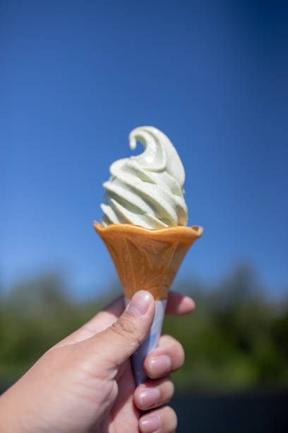 istock Hand holding Wasabi ice cream cone on blue sky background. 984725960