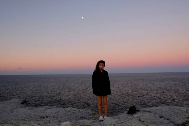 istock Chinese girl on cliff against dramatic sunset sky. 984732410
