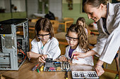 Happy teacher assisting school girls in repairing computer component in the classroom.
