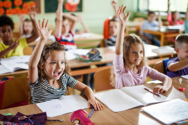 istock Happy school children raising their arms to answer the question on a class. 984738174