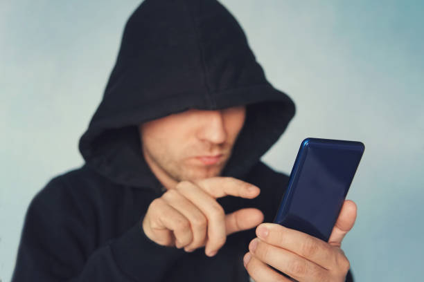 istock Faceless unrecognizable hooded person using mobile phone, identity theft and technology crime concept, selective focus on body, hacking a smartphone. identity theft. 984741248