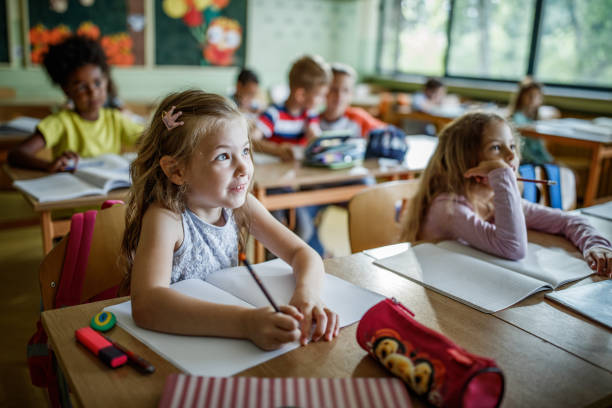 Elementary students paying attention during a class in the classroom. Happy schoolgirl paying attention during a class with her friends in elementary school. elementary school building stock pictures, royalty-free photos & images