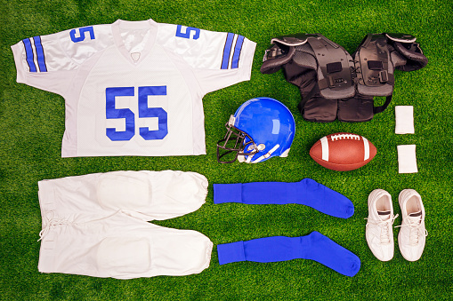 A flat lay arrangement of an Americam Football kit with ball, shirt, helmet and protective pads.