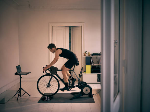 No gym, no problem Shot of a young man working out on an exercise bike at home exercise bike stock pictures, royalty-free photos & images