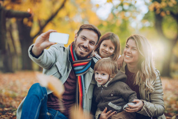 istock Happy family having fun while taking a selfie with mobile phone in the park. 984753262