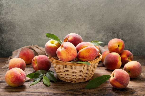 istock peaches with leaves in a basket on wooden table 984767282