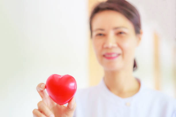istock Red heart held by smiling female nurse's hand, representing giving effort high quality service mind to patient. Professional, Specialist in white uniform concept 984772574