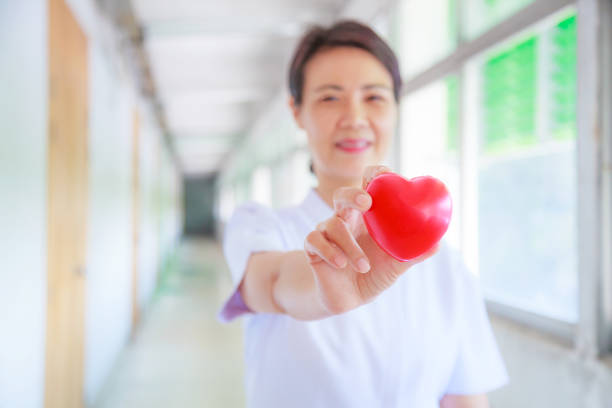 istock Red heart held by smiling female nurse's hand, representing giving effort high quality service mind to patient. Professional, Specialist in white uniform concept 984772628