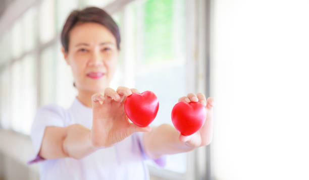 istock Red heart held by smiling female nurse's hand, representing giving effort high quality service mind to patient. Professional, Specialist in white uniform concept 984772642