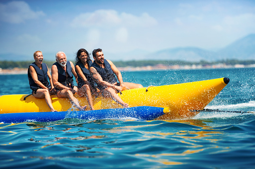 Closeup of senior couple with their children enjoying banana boat ride during their summer vacation.