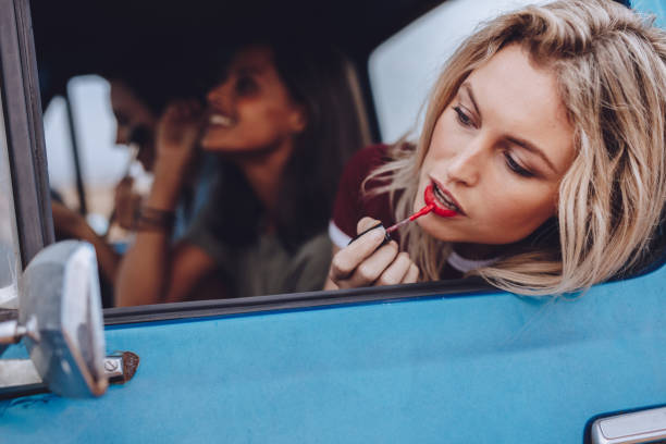 frauen auf roadtrip make-up in einem fahrenden auto zu tun - lippenstift stock-fotos und bilder