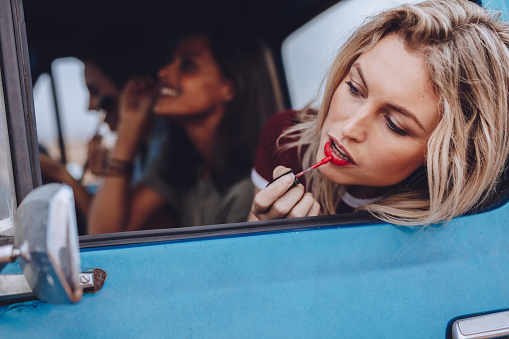 Three young woman going on a road trip. Female friends doing makeup in moving car.