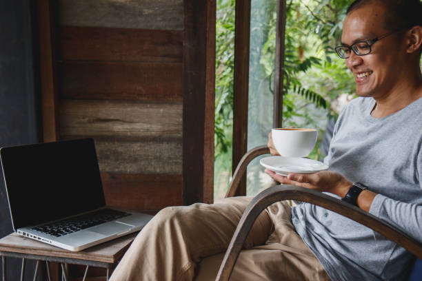 istock Cheerful asian male entrepreneur feeling happy about creating successful project drinking coffee while relaxing in resort. summer vacation holidays. 984792760