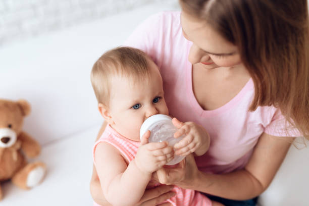 istock Young mother feeding baby milk bottle home. 984804122