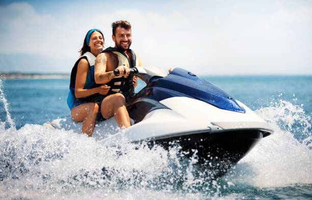 Jet skiing. Closeup side view of a young couple riding a jet ski on a sunny summer day at open sea. The guy is driving and the girls is sitting behind. neoprene photos stock pictures, royalty-free photos & images