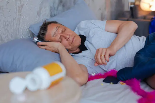 Morning sickness. Exhausted mature man resting in bed and holding bottle