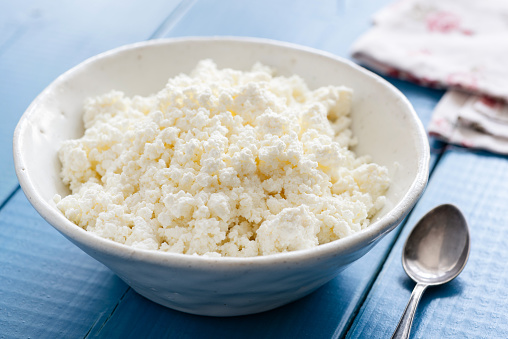 Ricotta or cottage cheese in white bowl on blue table. Healthy dairy product. Tvorog or farmer's cheese.