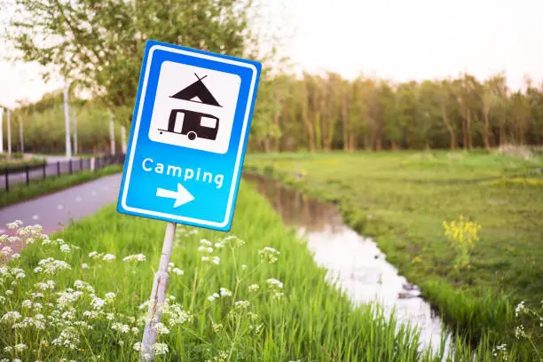 Photo of Camping sign in a countryside with a little river and green grass on background.