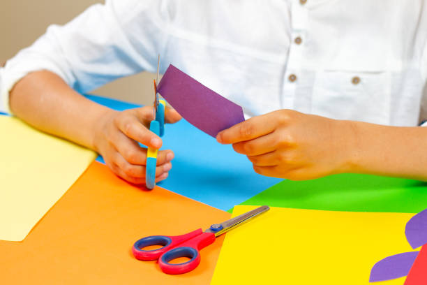 istock Child hands cutting colored paper with scissors at the table. 984864796