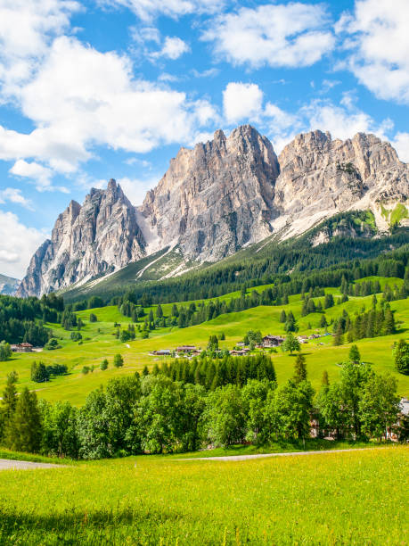 felsigen grat des pomagagnon berges über cortina d ' ampezzo mit grünen wiesen und blauem himmel mit weißen sommerwolken, dolomiten, italien - veneto stock-fotos und bilder