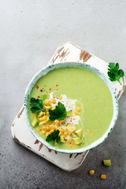 istock Homemade tender soup puree from avocado and corn with cream in rustic ceramic plate on gray concrete old background. Selective focus. Top view. Copy space. 984969040