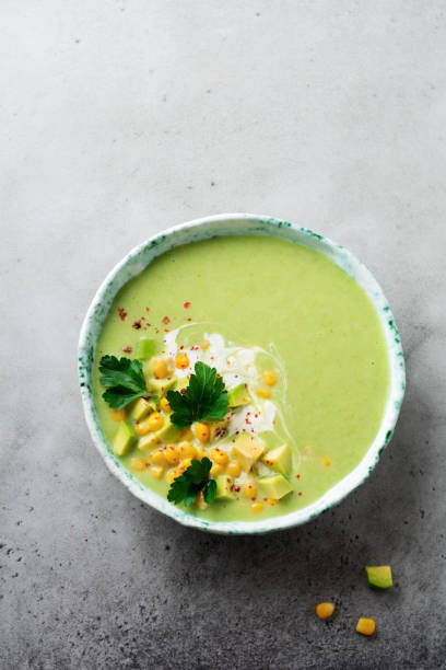istock Homemade tender soup puree from avocado and corn with cream in rustic ceramic plate on gray concrete old background. Selective focus. Top view. Copy space. 984971342